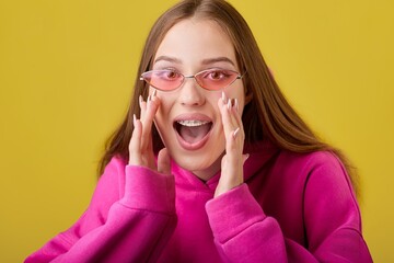Image of cheerful young female with braces on teeth shouting joyfully with hands near mouth....