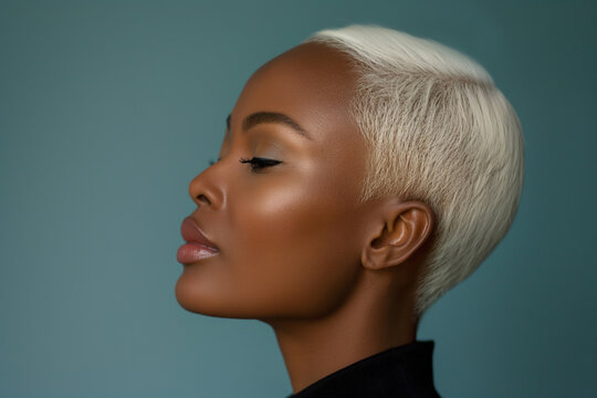 Profile of a woman with a platinum buzz cut, dramatic winged eyeliner, posed against a soft teal background