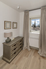 A room with a wooden dresser of drawers, a square window with views and a radiator under the window