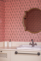Bathroom with cream marble countertop, gold-framed mirrors, pink wallpaper, and white porcelain sink