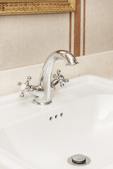 White porcelain sink on a cream marble countertop with a vintage-style chrome faucet and a...