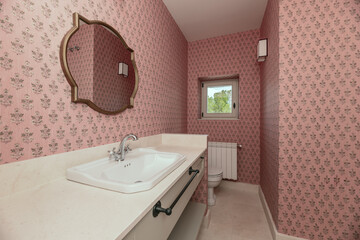 Bathroom with cream marble countertop, gold-framed mirrors, pink wallpaper, square aluminum window and white porcelain sink