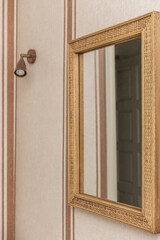 a mirror with a wicker frame on a wall with decorative paper and a small wall light with an LED bulb