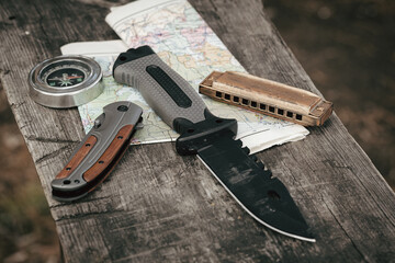 Knife, compass, harmonica and map on a wooden table. Concept of travel and adventure.