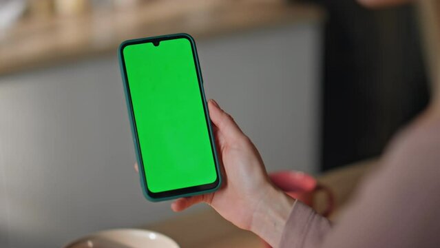 Woman reading chromakey smartphone message sitting home kitchen close up. 