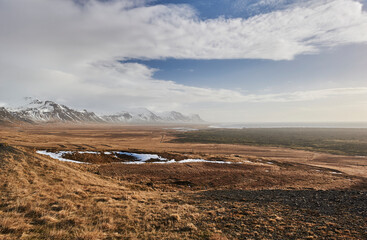 Northern landscapes: The rugged expanse of Staðarsveit coast unfolds beneath a wide sky, with Iceland's dramatic mountain ranges in the distance. Snæfellsnes peninsula (region of Vesturland, Iceland)