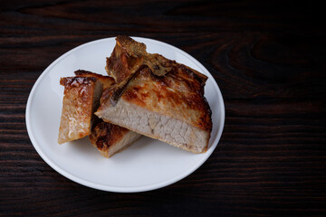 Roasted pork entrecote cut into pieces in a white plate on a wooden cutting board . Grilled pork...