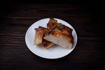 Roasted pork entrecote cut into pieces in a white plate on a wooden cutting board . Grilled pork...