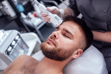 Closeup of face of beautiful relaxing man undergoing hardware cosmetology procedure in spa