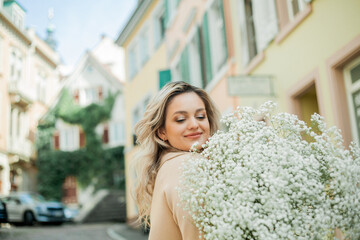 Portrait of beautiful young blonde woman with bouquet of white flowers in the center of European...