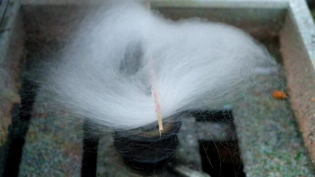 Close-up of white cotton candy threads being spun in a traditional spinning machine. Sugar floss forming fluffy texture. Street snack preparation with spinning sugar process