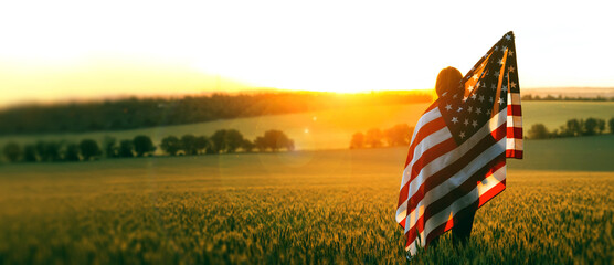 Independence Day. Beautiful girl with the American flag in a wheat field at sunset. 4th of July....