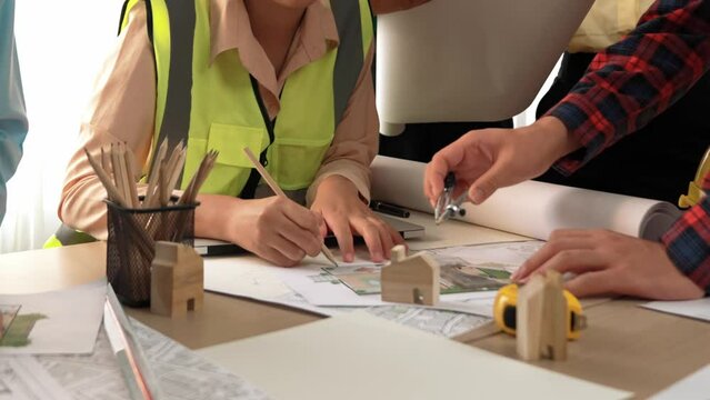 Smart architect and safety engineer discussion about building blueprint on table with architectural document, measurement tools and wooden block scatter around at modern office. Closeup. Delineation.
