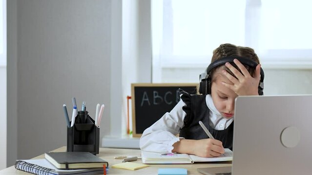 Caucasian child girl wear headphones, using laptop sitting writing listening tutor online virtual lesson