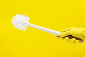 Hand in yellow rubber glove holding a cleaning brush on a yellow background.