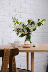Spring morning in light room: bouquet of white flowers, cake, glass of green tea.