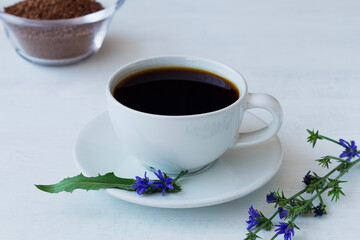 delicious chicory drink in white Cup decorated blue chicory flowers with Ground chicory root on a wooden spoon on white background. hot and healthy drinks. coffee substitute. copy space.