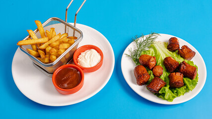 Fries basket and fried sausage pieces on plate