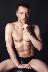 Fototapeta premium A man with a beautiful body poses in the studio against a black background.