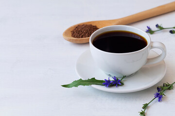 chicory drink in white Cup decorated blue chicory flowers with Ground chicory root on a wooden spoon on white background. hot and healthy drinks. coffee substitute. copy space.