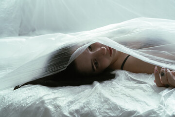 Young Woman Lying Under a Sheer Fabric on a Bed