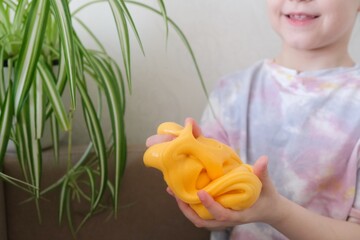 Girl stretching yellow slime to the sides. Kids hands playing slime toy. Trendy liquid toy to hands...