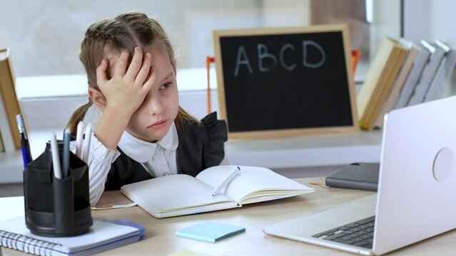 Disappointed girl slapping head with hand while sitting at desk with laptop