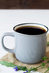 close-up of chicory drink in Grey Cup and blue chicory flowers on white table with sackcloth. hot and healthy drinks. coffee substitute. copy space. vertical