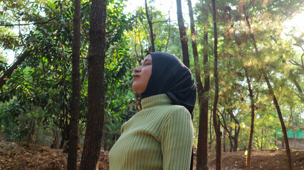 Happiness concept. Arab Woman eyes closed and breathing fresh air at pine forest with sunlight.
