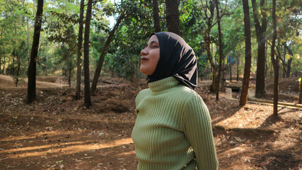 Happiness concept. Arab Woman eyes closed and breathing fresh air at pine forest with sunlight.