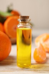 Bottle of tangerine essential oil and fresh fruits on white wooden table, closeup