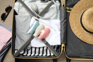 Plastic bag of cosmetic travel kit and clothes in suitcase, top view