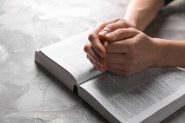 Religion. Christian woman praying over Bible at gray textured table, closeup