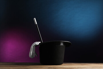 Magician's hat, gloves and wand on wooden table against dark background