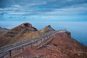A rocky cliff overlooks the ocean with a fence leading to the water. The scene is serene and...