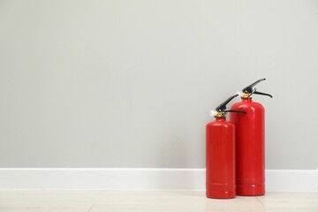 Fire extinguishers on floor near light grey wall, space for text