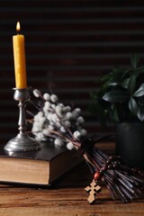 Rosary beads, Bible, burning candle and willow branches on wooden table, closeup
