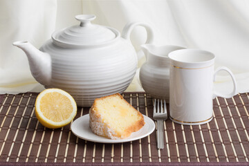 a round lemon cake with a crumble top cut into slices with a tea pot and mug on a wooden table