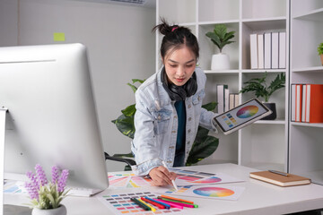 Female designer wearing headphones listening to music while doing graphic design work Choose colors for working with the computer at the table.