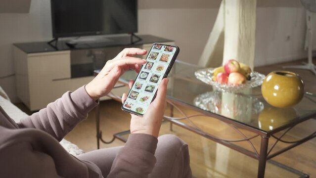 Ordering dishes in a restaurant online using a smartphone. Woman selects dishes from the internet menu of a restaurant online, using an application on a smartphone.