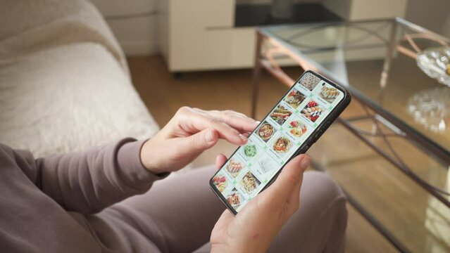  Ordering food using a smartphone at home. Woman selects sushi sets in the internet menu of a Japanese restaurant using an application on a smartphone. 