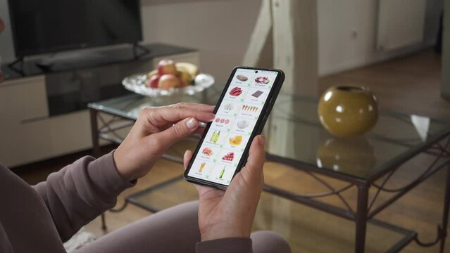 Ordering food using a smartphone at home. Woman selects market food in an online store using an application on a smartphone. 
