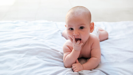 Banner with infant baby lies on his stomach and sucks his thumb, looks at the camera and laughs. Bright emotions of a baby, a joyful little girl lies on a blanket in a diaper. Mothers Day.