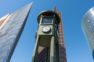 An old tower on which a clock and a traffic light are located against the backdrop of modern tall...