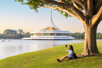 Beautiful woman using smart phone and resting at Suan Luang Rama IX Park. People enjoy and relax at...