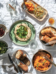 spread of multiple traditional mediterranean dishes on white linen, including beans, olives, bread and hummus