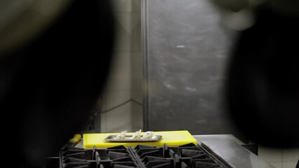 Side view of a confident professional chef in a black uniform sprinkles a finished dish with cheese while cooking in the kitchen in a restaurant