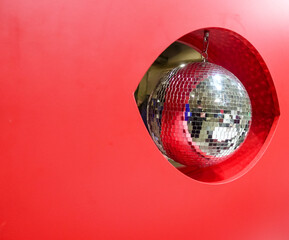 Round mirror disco ball. It is in the red hole, which is part of the red wall. The mirror ball...