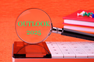OUTLOOK 2025 through a magnifying glass on a calculator on an orange background