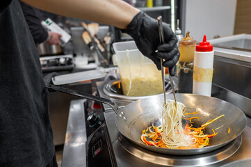 chef hand cooking Noodle with vegetables on restaurant kitchen